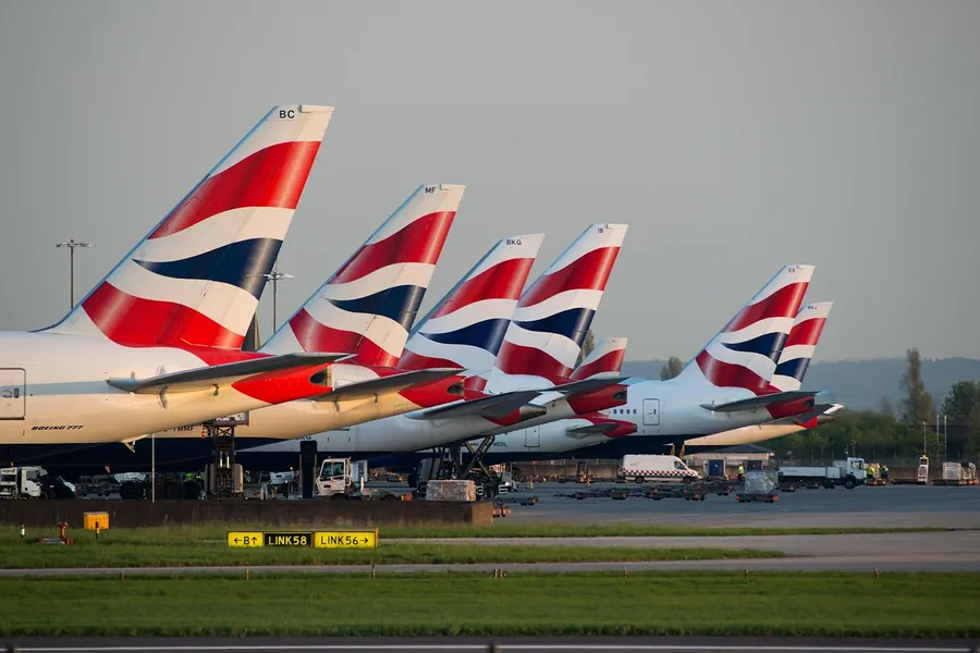 A row of airliner tail fins lined up at an airport stand under a grey sky