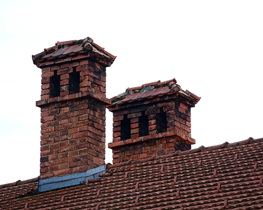 Two old brick chimney stacks with decorative tops rising from a clay tile roof, the kind of detail a roofer should survey closely in Isleworth