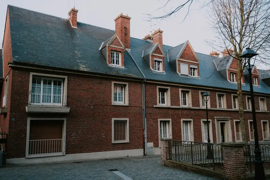 Red-brick building with a row of gabled dormers and tall chimney stacks on a grey slate roof