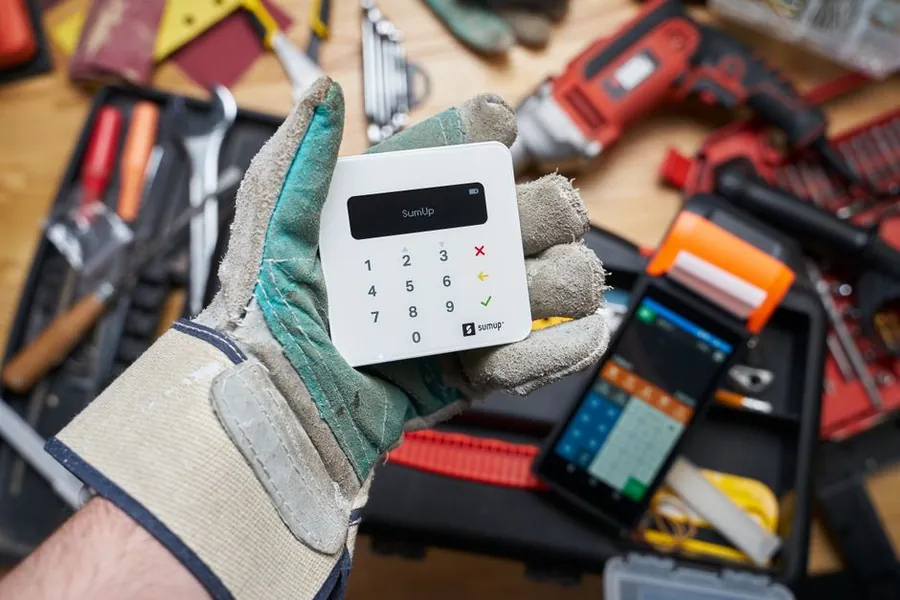 Roofer in worn work gloves holding a card reader, taking payment for an emergency roof call-out