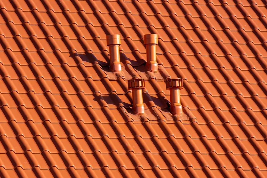 Orange clay roof tiles in hard midday sunlight with sharp shadows across the slope