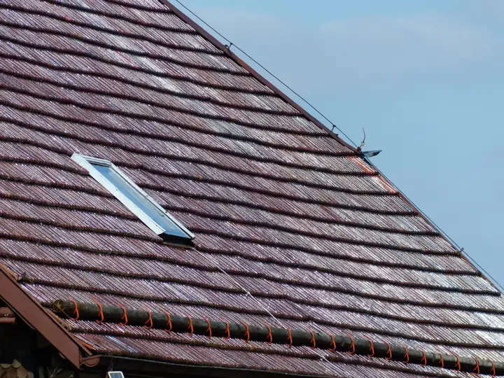 Close-up of a pitched roof of brown tiles with a small rooflight set into it