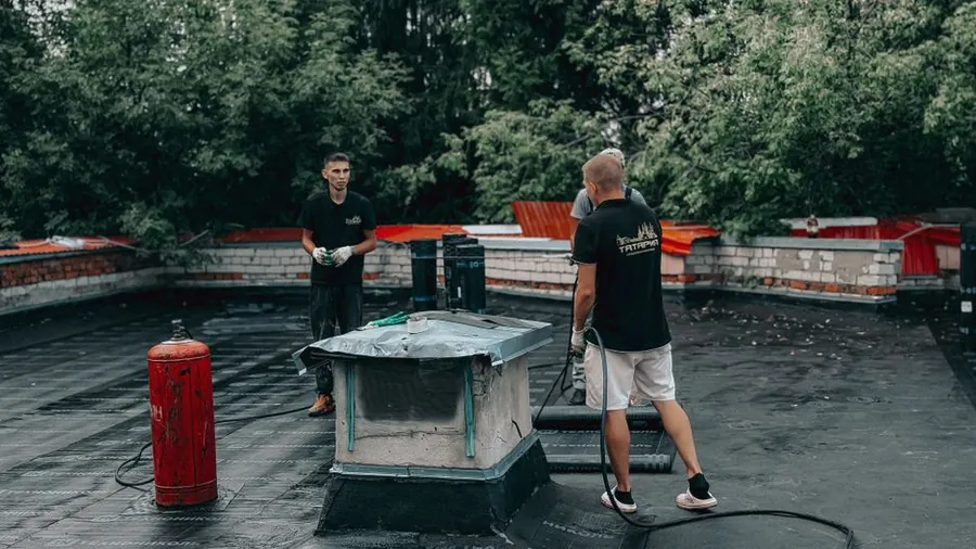 Roofers carrying out maintenance on a small flat roof deck above a converted loft