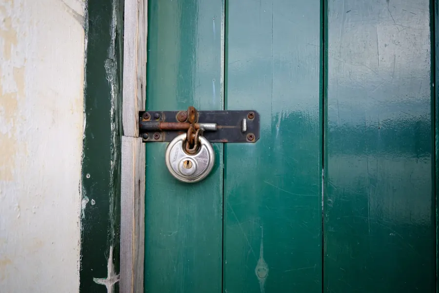 Padlocked green timber garage door on an old brick garage