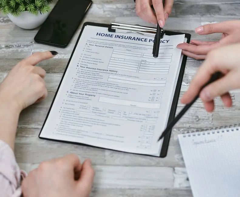 Hands going through a home insurance form on a clipboard beside a phone