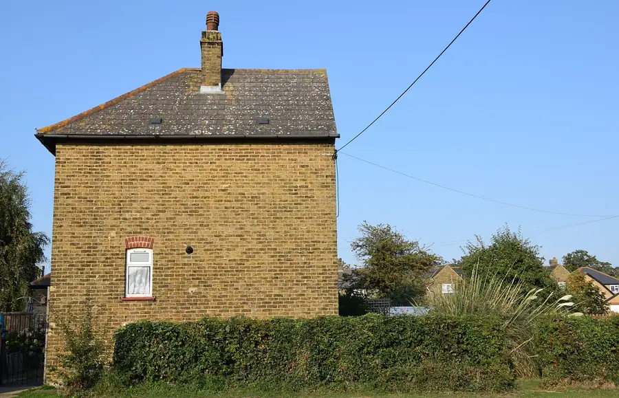 Yellow stock brick house end with a pitched tiled roof and a brick chimney stack at the ridge, against a clear blue sky