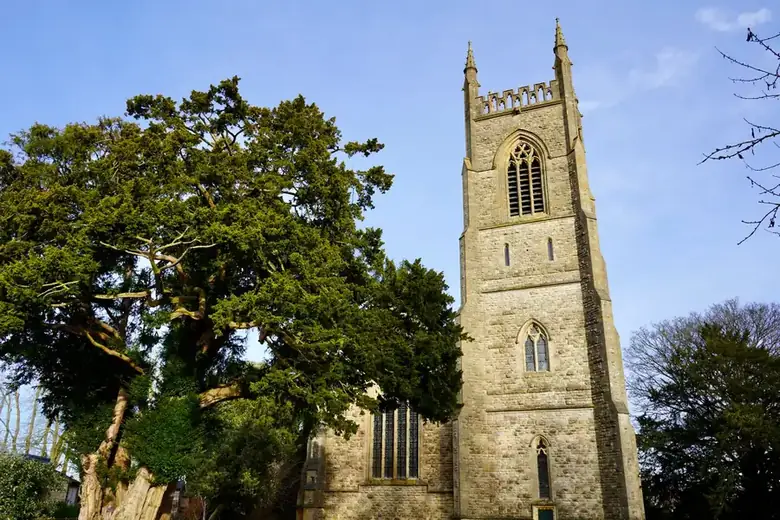An old English stone church beside a large yew tree, similar in setting to St Mary's at Bedfont Green conservation area