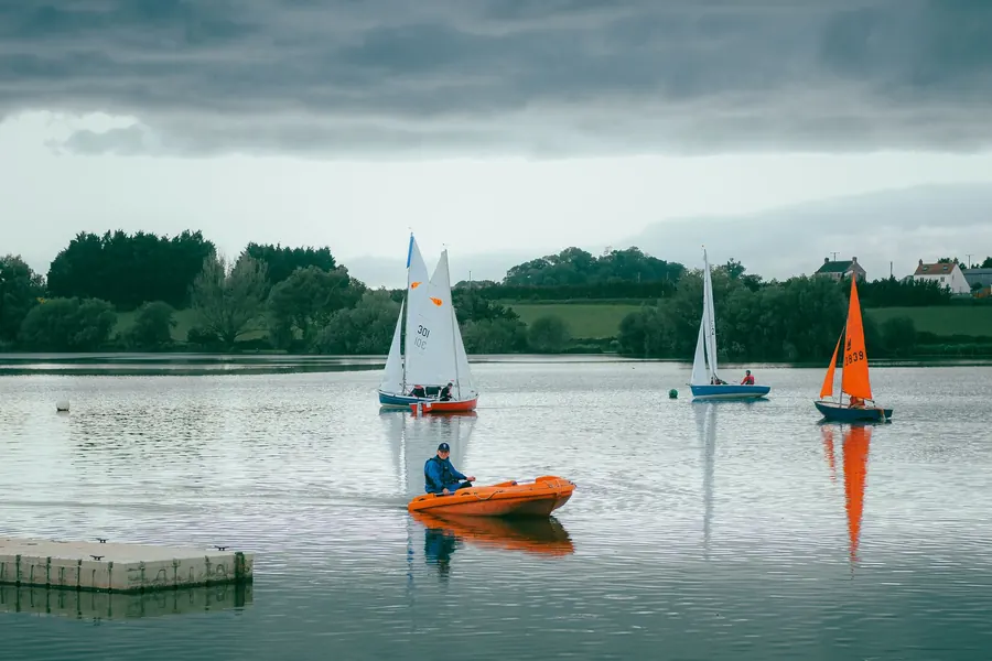 Sailing dinghies on open water under a grey sky, like the exposed reservoirs and lakes west of Feltham and Bedfont