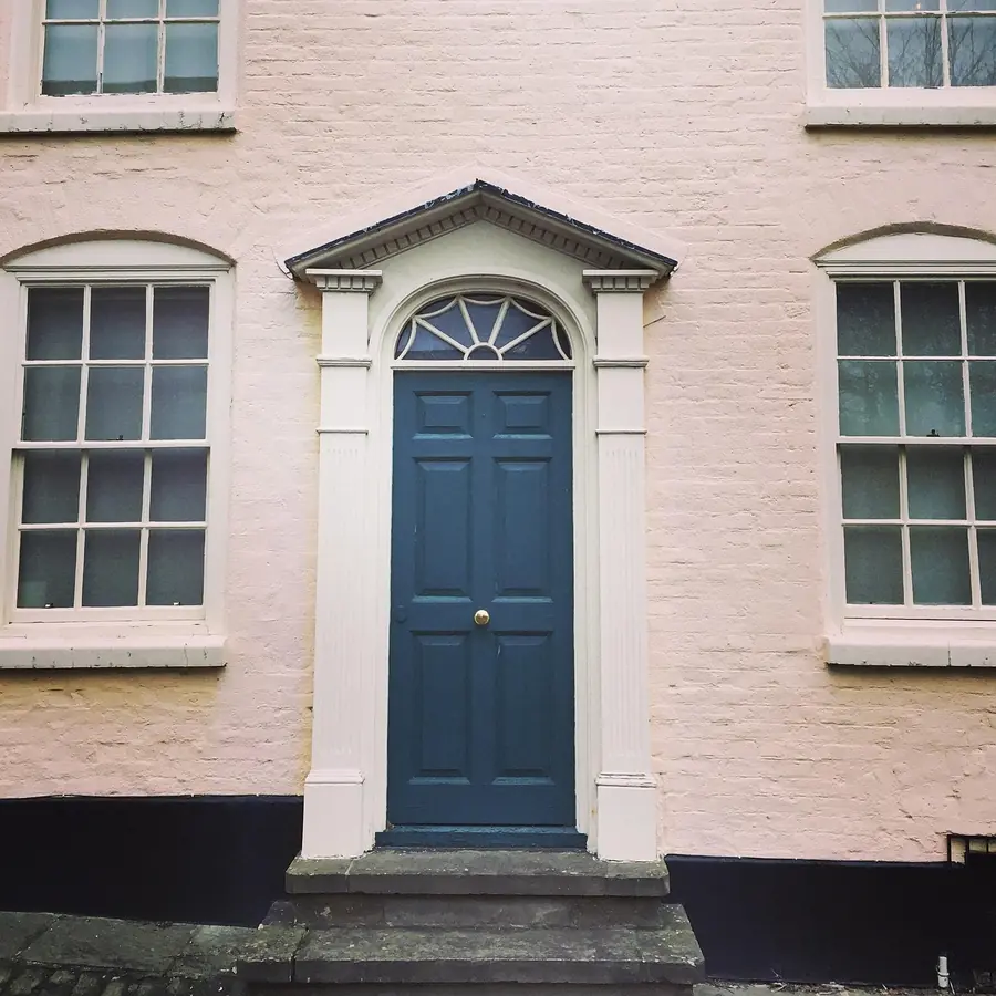Painted brick house front with a dark blue panelled door under a classical doorcase, between two sash windows