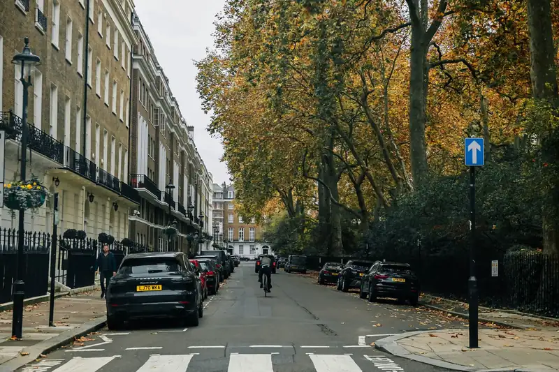 Cars parked along both sides of a tree-lined residential street in west London