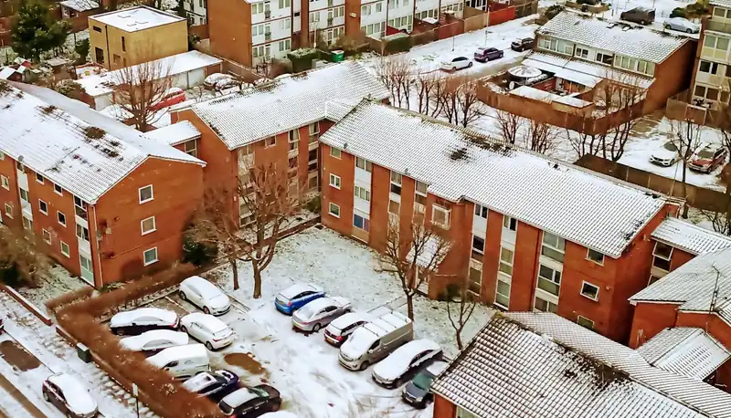 Purpose-built brick blocks of flats around a shared car park, where the roof over every top-floor flat belongs to the freeholder and is repaired through the service charge