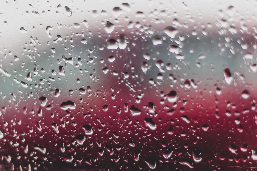 Raindrops running down a window pane with blurred colours behind the glass