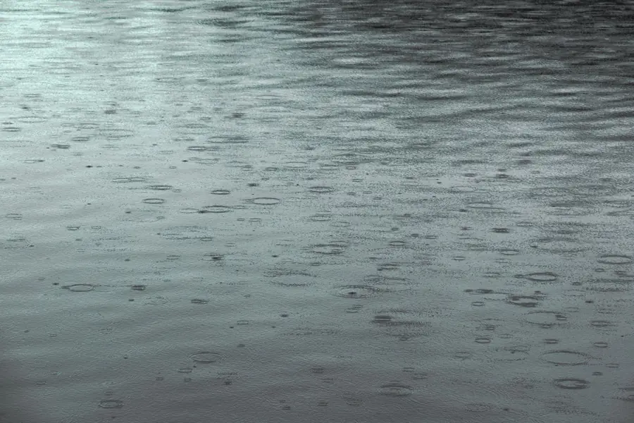 Rain falling into a shallow pool of standing water on a flat surface