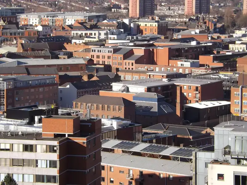 Rooftops of red-brick blocks of flats and older buildings across a British city, some flat-roofed and some pitched