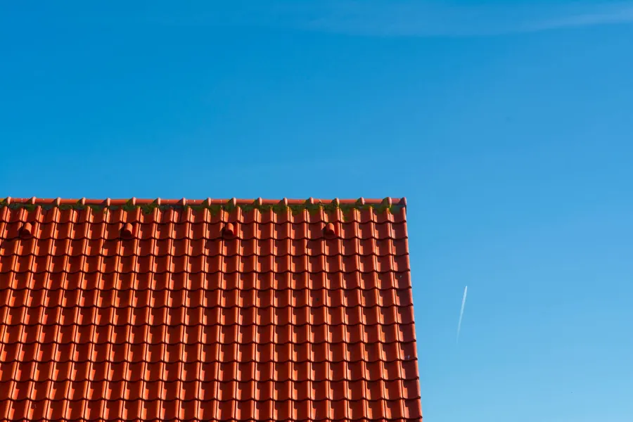 A red tiled roof against a clear sky with an aircraft contrail overhead, as seen under the flight paths around Bedfont