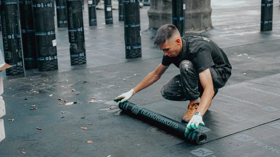 Roofer rolling out a new waterproof lining along a roof gutter