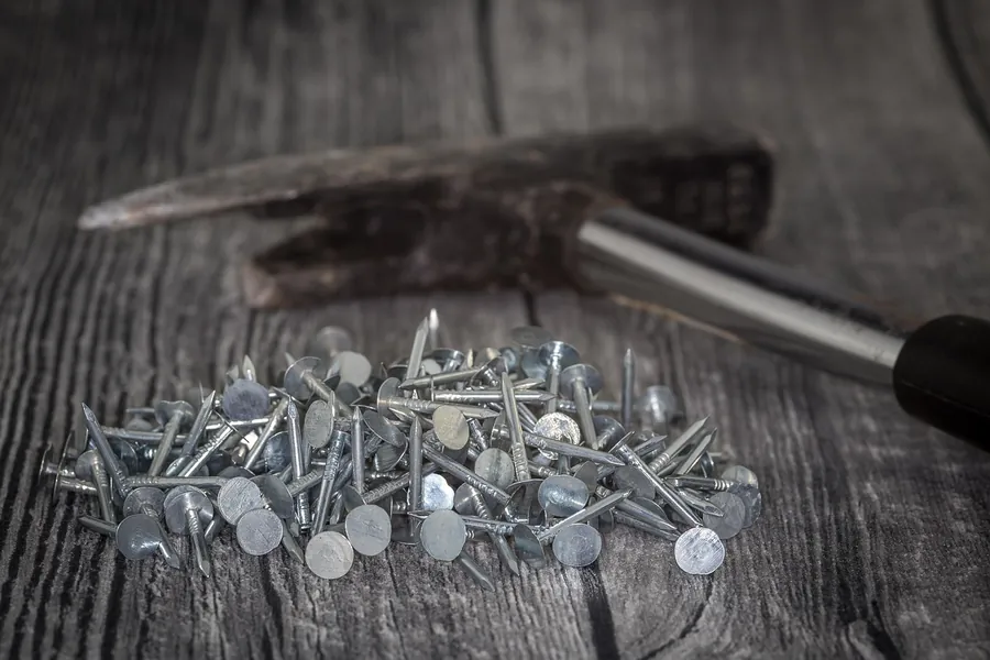 Roofing hammer resting beside a pile of galvanised clout nails on a dark wooden bench