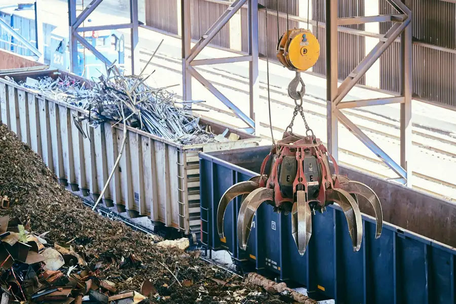 Grab crane lowering scrap metal into a railway wagon at an industrial recycling yard
