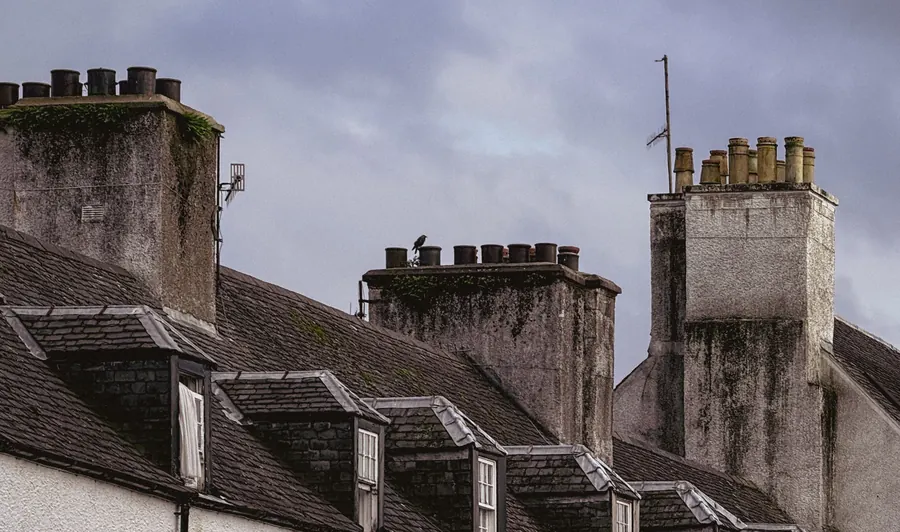 Tall shared chimney stacks carrying several clay pots, rising between the slate roofs and dormer windows of a terrace