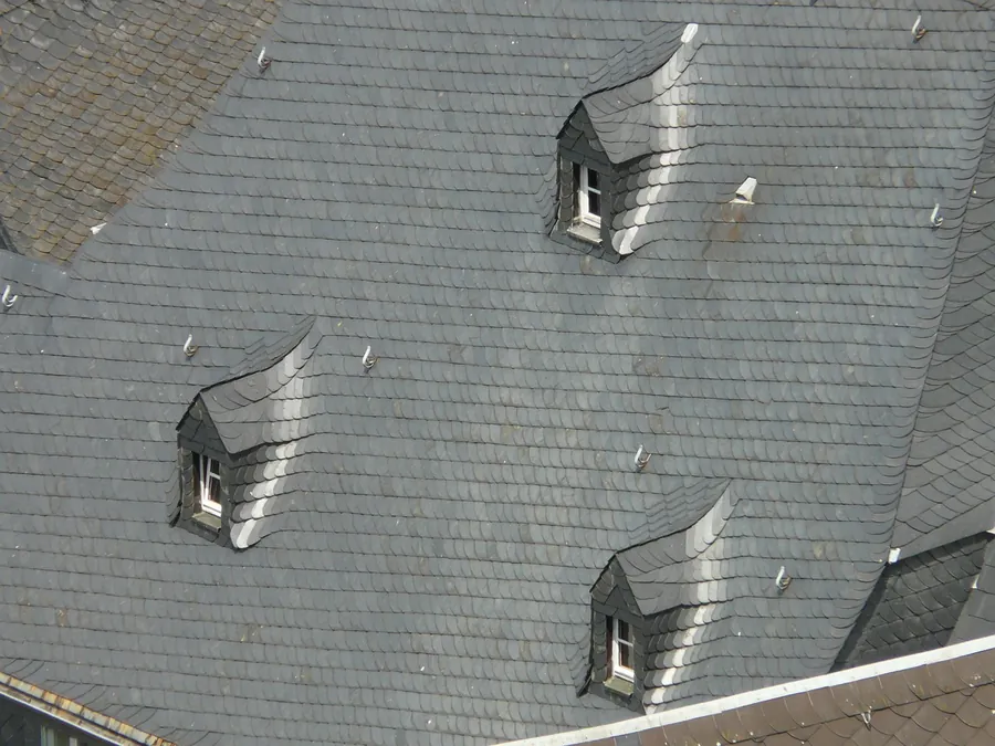 Grey slate roof seen from below with three small dormer windows, their metal cheeks and flashings catching the light