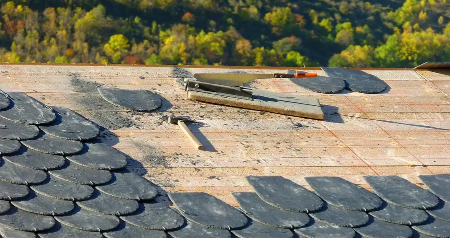Slates partly stripped from a roof with old battens exposed and tools resting on the slope, the kind of strip and re-lay priced on Isleworth terraces