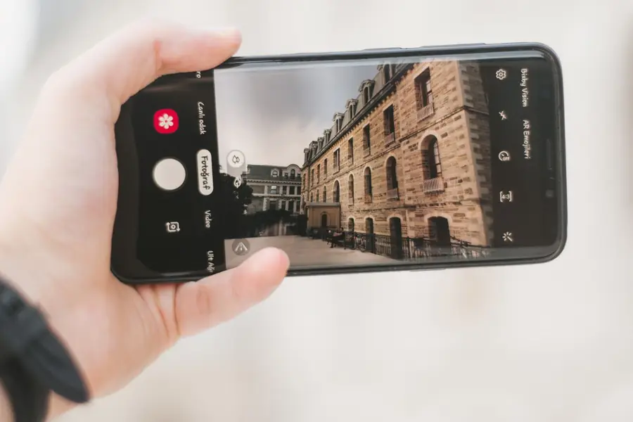 Hand holding a smartphone up to photograph the outside of a building as evidence