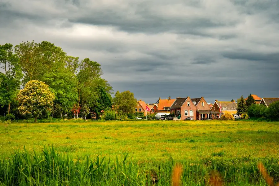 Dark storm clouds gathering over houses beyond a green field