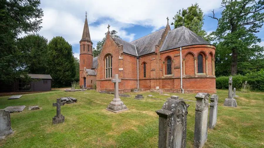 Victorian red-brick church with a slate roof and small spire behind an old graveyard