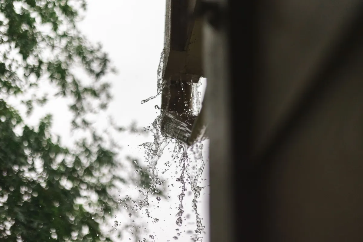 Rainwater spilling past a failed gutter during heavy rain
