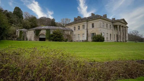 Elegant Regency manor house with classical columns seen from formal parkland