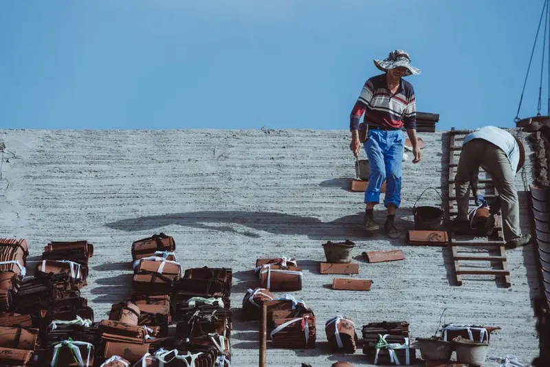 Roofers at work re-tiling a pitched roof, new clay tiles stacked in rows